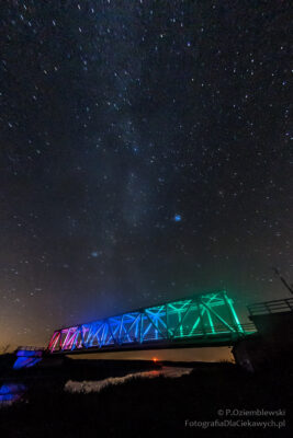 Gwiazdy na niebie nad mostem kolejowym oświetlonym różnymi barwami